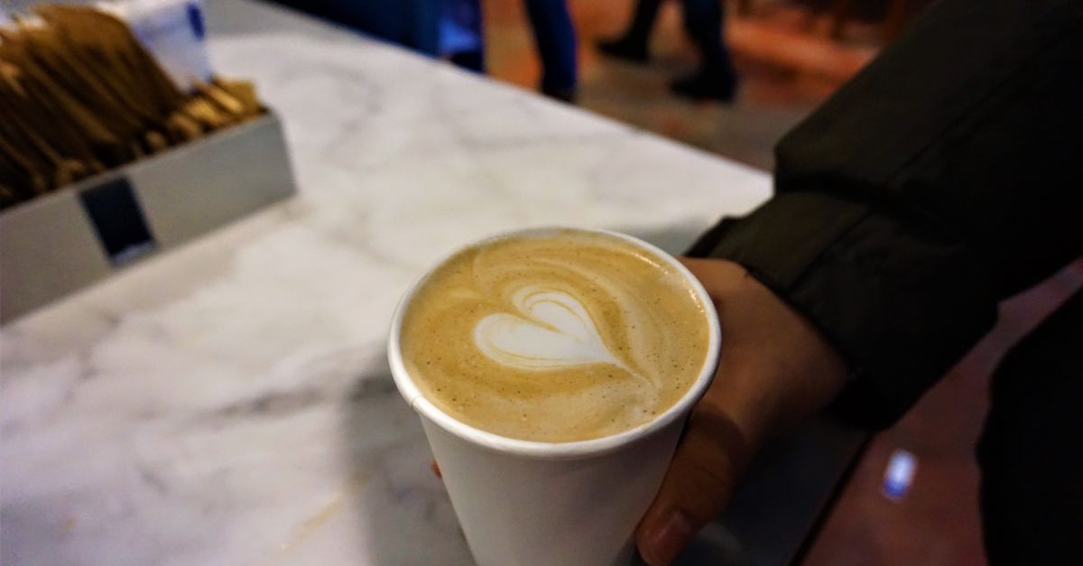 A hand holds a cup of coffee with elegant latte art on a marble countertop in a cozy cafe.